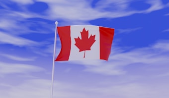 The Canadian flag with a red maple leaf at the center, flanked by two vertical red bands on a white background, is waving in a clear blue sky with scattered clouds.