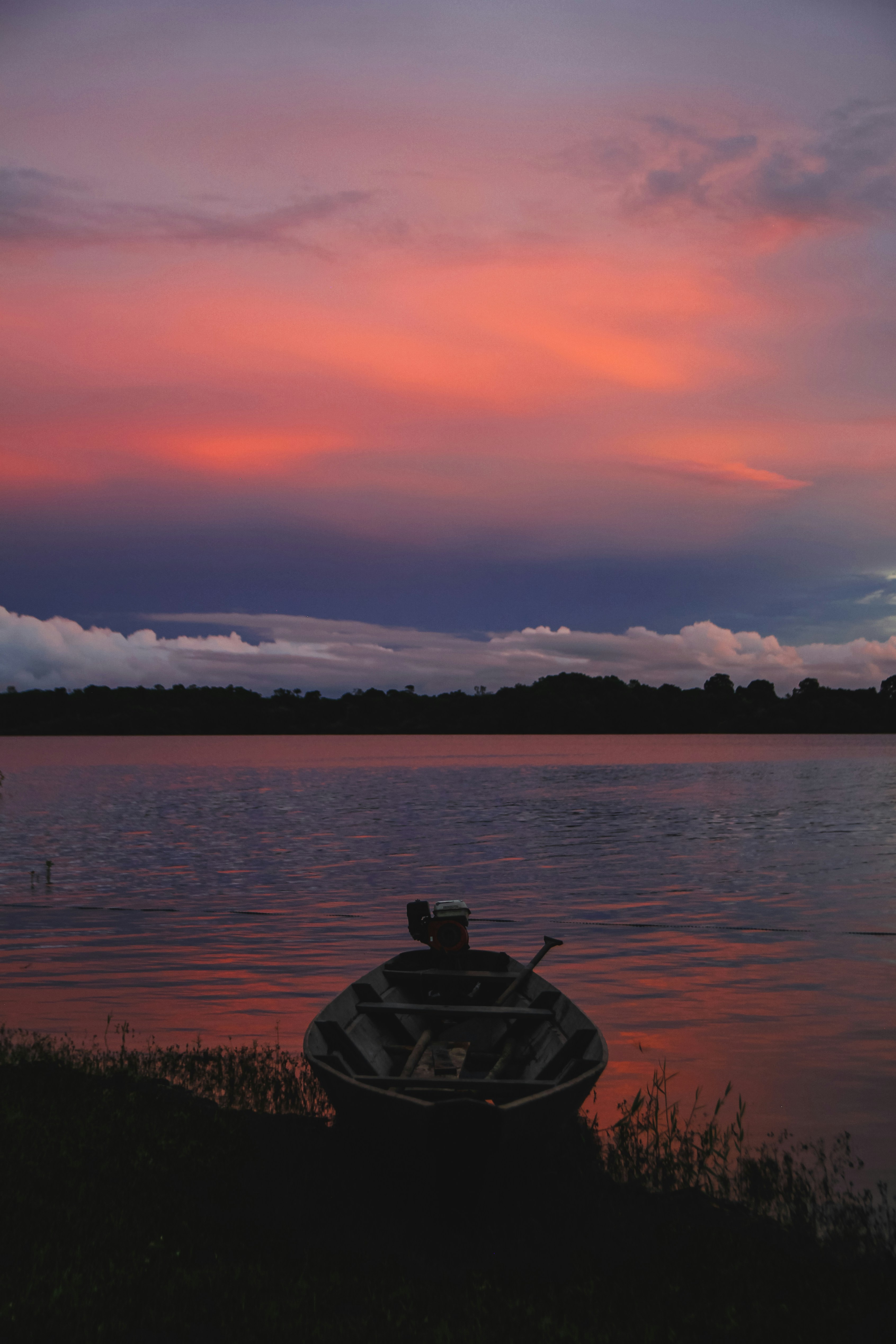 a boat sitting on the shore of a lake at sunset