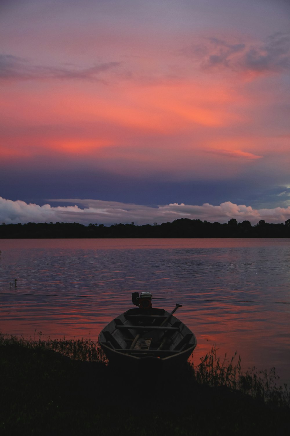 a boat sitting on the shore of a lake at sunset