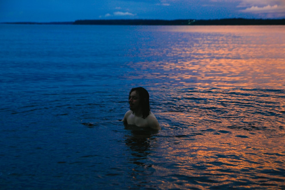 uma mulher em um corpo de água ao pôr do sol