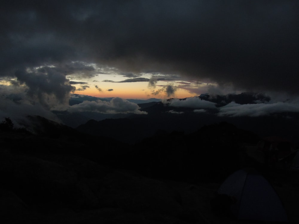 a dark sky with clouds and a tent in the foreground