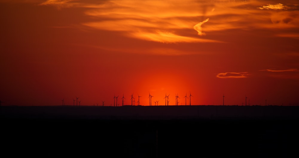 the sun is setting over a field of wind mills