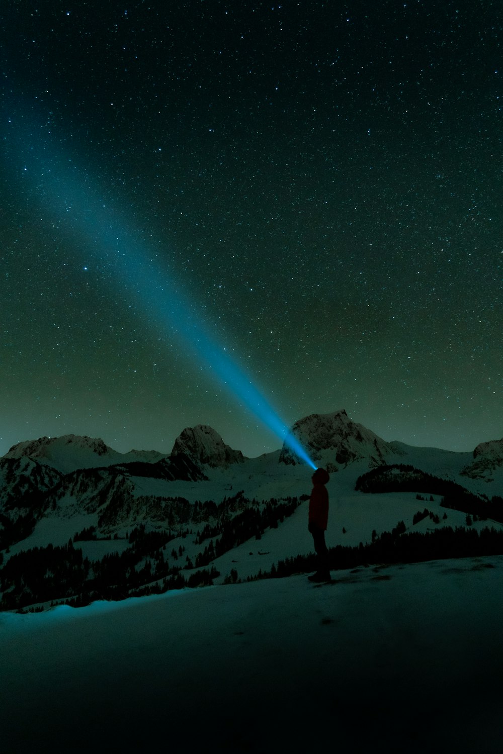 a person standing on top of a snow covered slope under a sky filled with stars