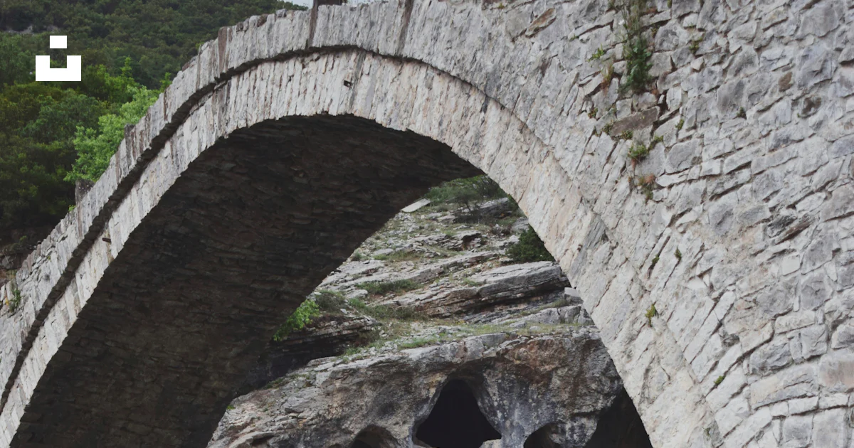 A stone bridge over a river surrounded by rocks photo – Free Grey Image ...