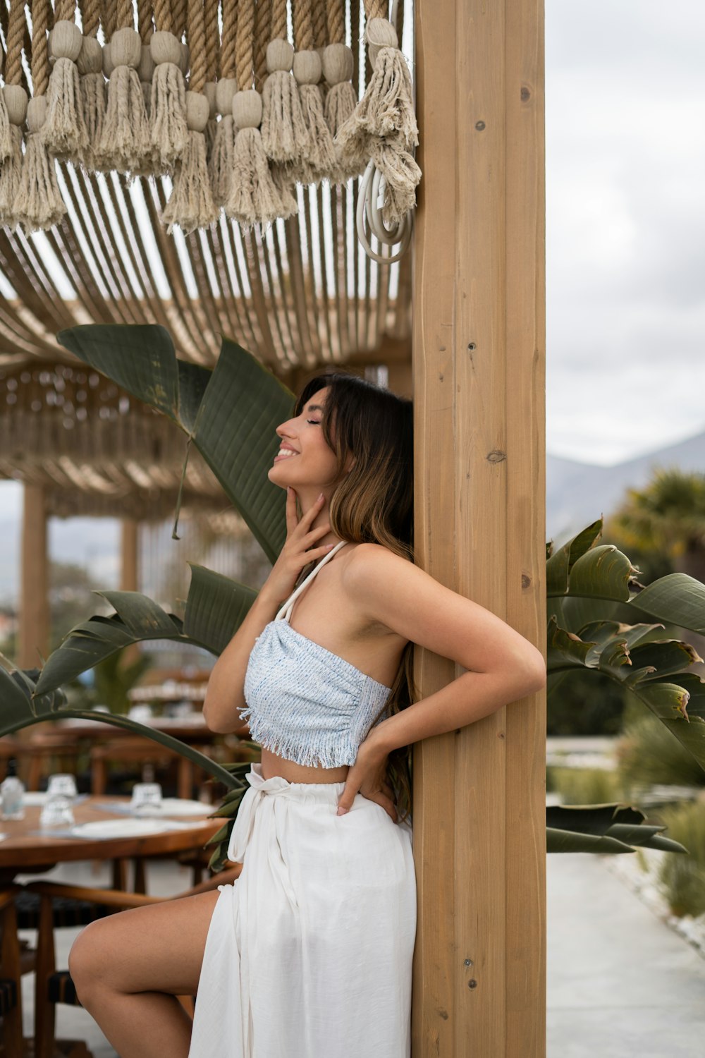 a woman in a white dress leaning against a wooden structure