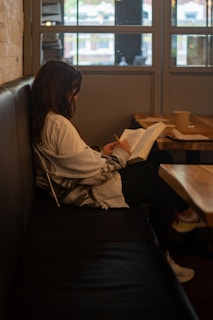 a woman sitting in a booth reading a book