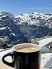 An open travel journal beside a cup of coffee with a scenic mountain view outside.