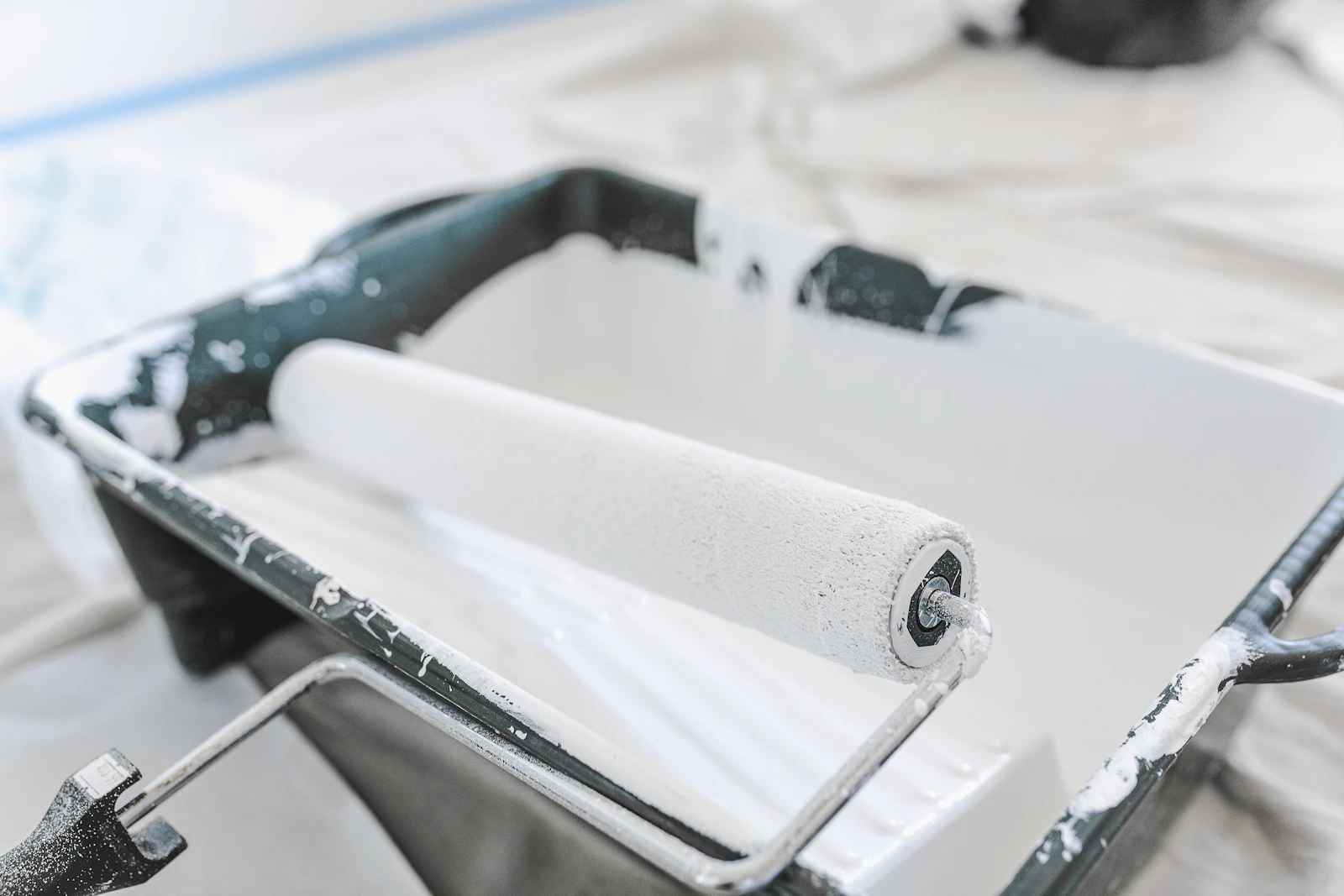 Paint roller resting in a tray of white paint on a dust sheet