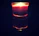 Close-up of a lit minimalist glass candle casting warm shadows in a dark room.