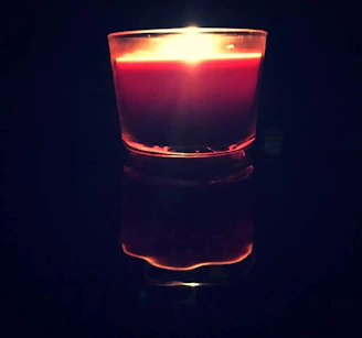 Close-up of a sleek, black-tinted luxury candle glowing softly against a cream background.