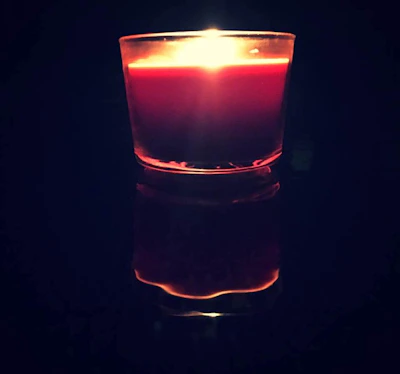 Close-up of a sleek, black-tinted luxury candle glowing softly against a cream background.