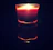 Close-up of a lit minimalist glass candle casting warm shadows in a dark room.