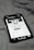 A smartphone displaying a social media profile screen rests on a fabric surface. The profile appears to belong to someone named Chris TDL with follow and following counts. The screen is centered in the image with a grayscale filter applied, and the edges of the phone case are visible.