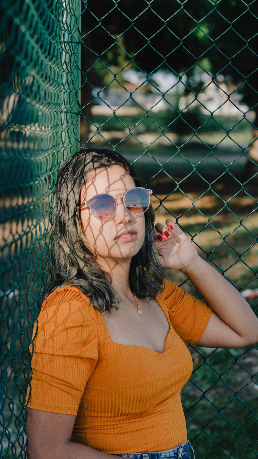 a woman leaning against a fence wearing sunglasses