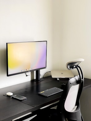A minimalist office setup featuring a charcoal grey ergonomic chair and a wood-toned work desk.