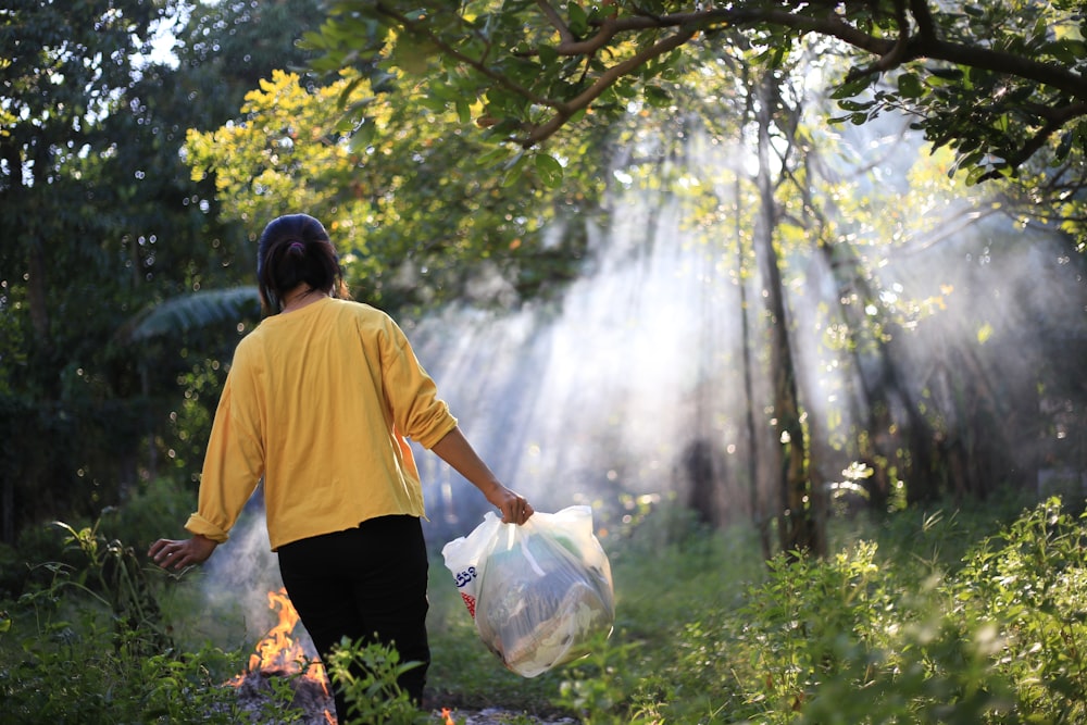 a woman walking through a forest carrying a bag of garbage