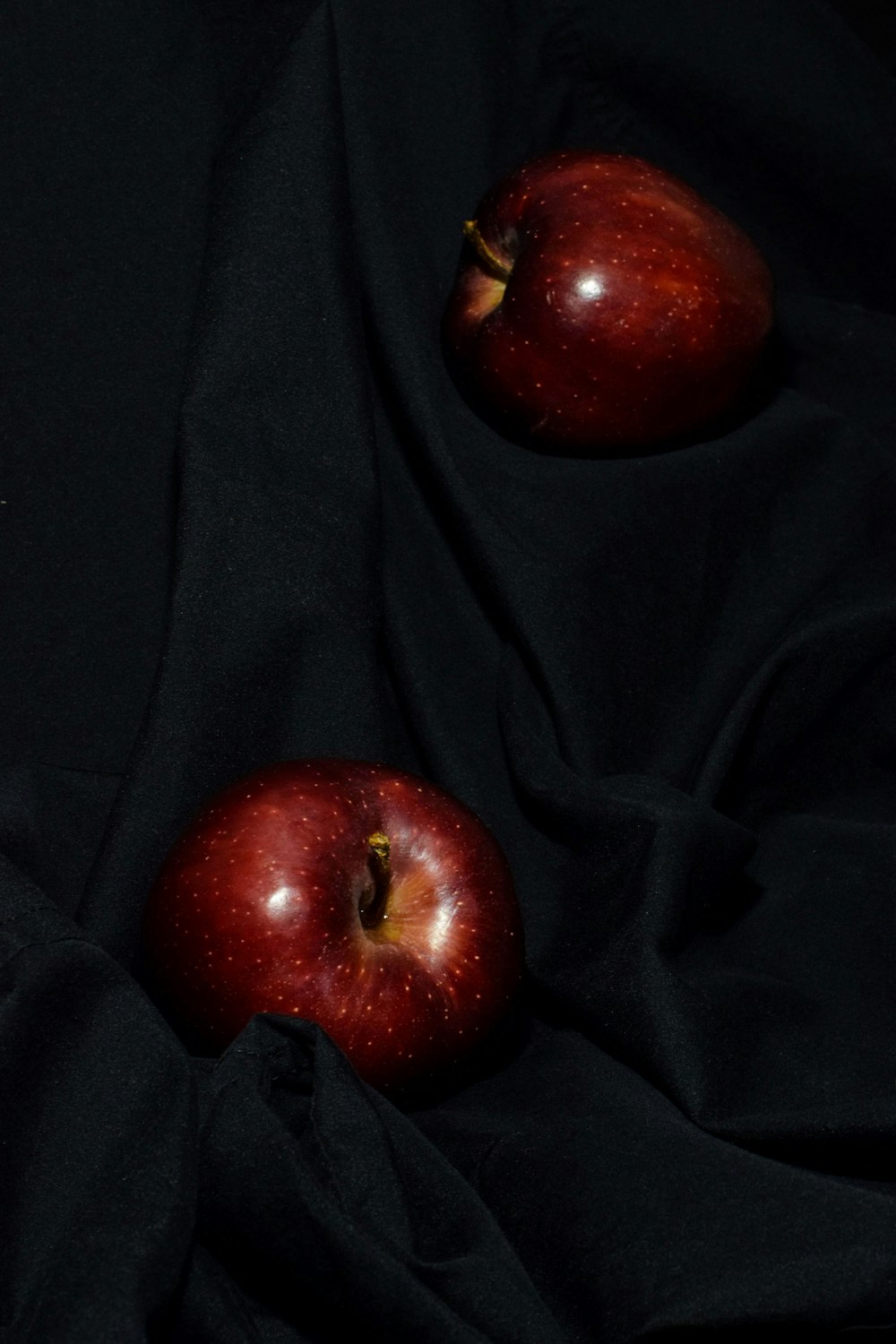 two red apples sitting on top of a black cloth