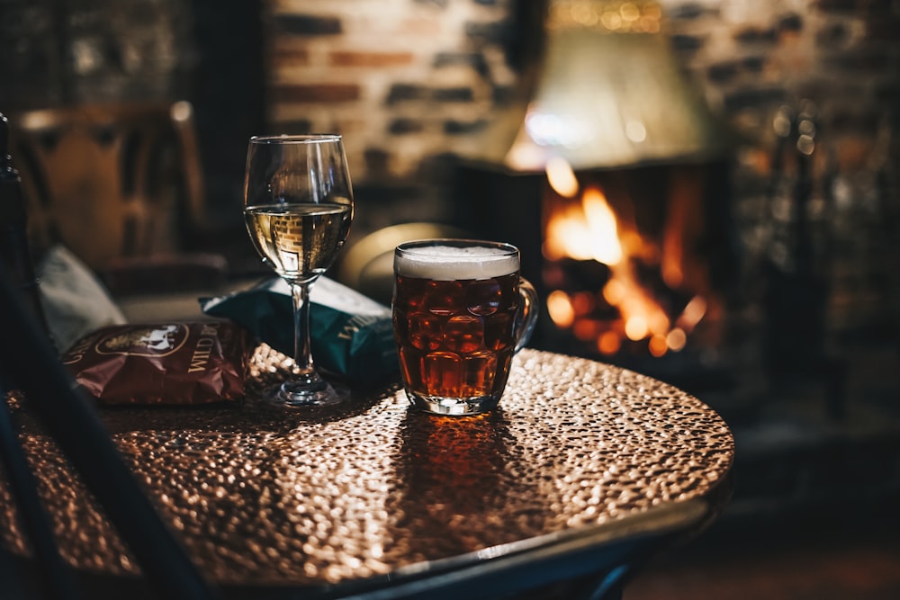 two glasses of beer sitting on a table in front of a fireplace