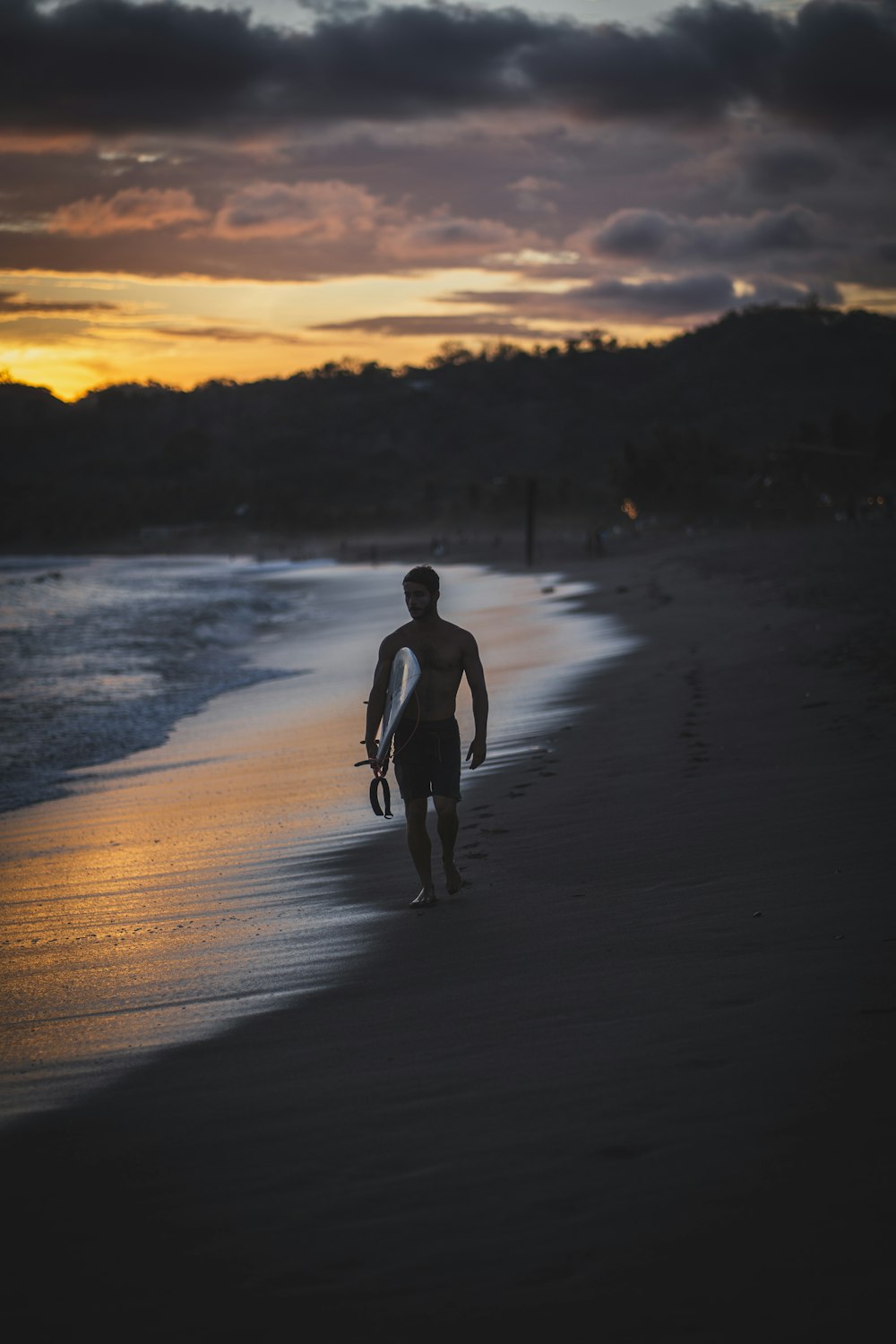 a man walking along a beach holding a surfboard