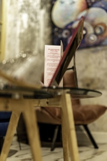 A focused view of a menu or a similar standing card on a glass table. Behind the table, there is an abstract artwork featuring circular shapes in various colors, set against a textured wall. The setting appears to be indoors, perhaps in a cafe or a lounge.