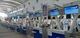 A series of check-in counters at an airport, specifically for economy class passengers. The counters have digital displays with flight information and signage for Malaysia Airlines. The architecture includes a modern design with high ceilings and plenty of natural light.