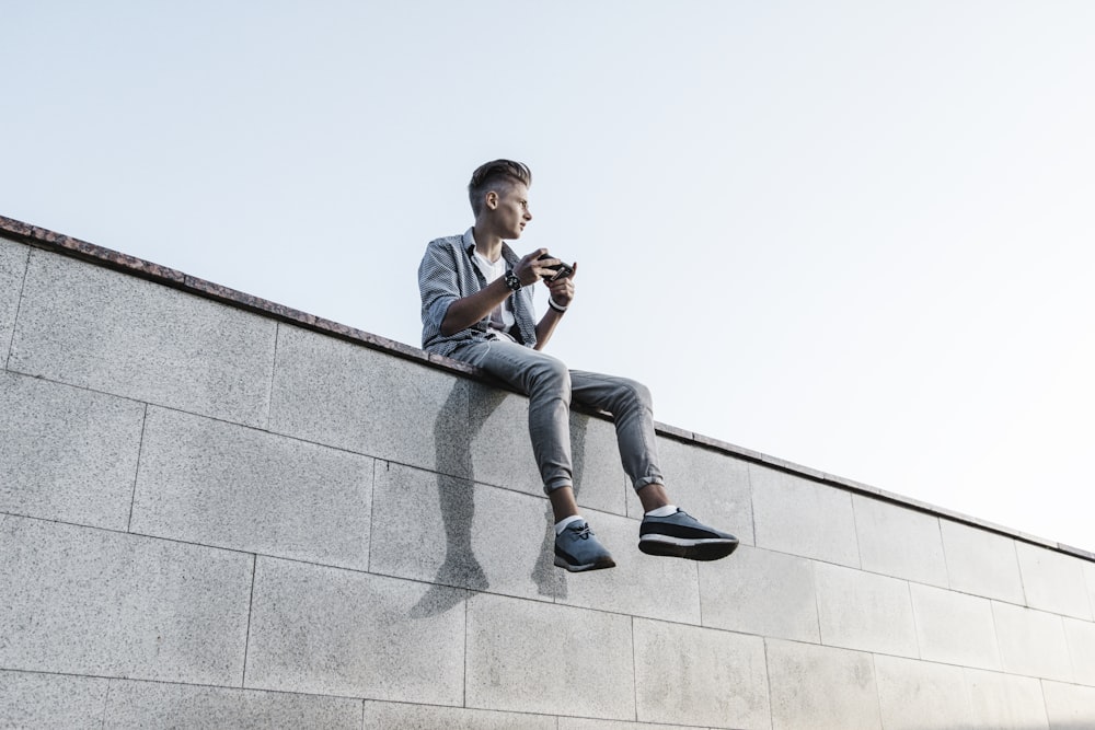 a man sitting on a wall looking at his cell phone