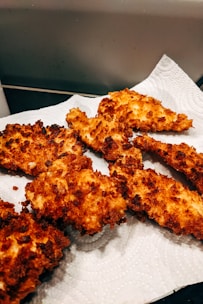 Crispy, golden-brown fried chicken pieces laid out on a white paper towel absorbing excess oil.