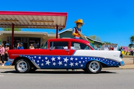 A classic American car displayed on a vibrant red, white, and blue themed show board.