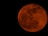 A large, bright full moon with a reddish hue dominates the dark night sky. The surface details of the moon including its craters are clearly visible, giving it a textured appearance.