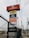 A tall signage tower displays multiple brand logos and names. Brands like Autopits, Pennzoil, Michelin, Kumho Tyre, Energizer, and others are shown on individual panels stacked vertically. The structure is surrounded by a black wire fence, with power lines visible in the background, set against a cloudy sky.