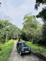 a jeep driving down a dirt road next to a lush green forest