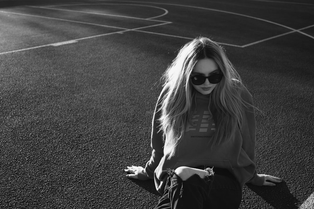 a woman sitting on a basketball court wearing sunglasses