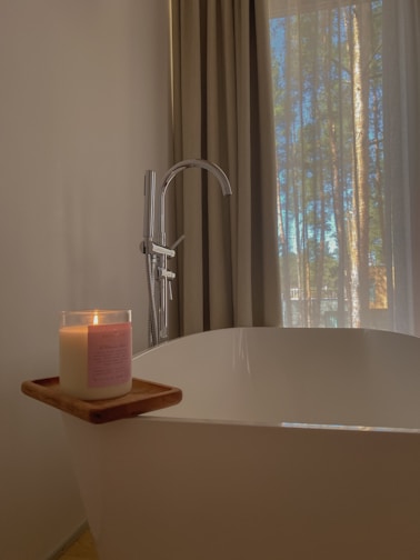 a candle sitting on top of a bathtub next to a window