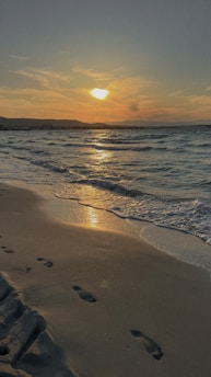 A serene beach sunset with footprints in the sand, symbolizing memories made during travels.