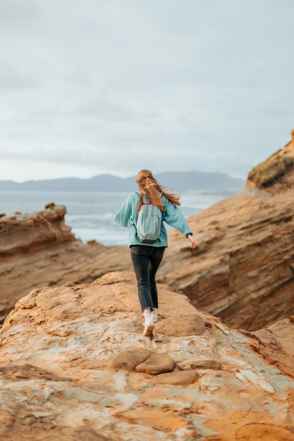 a woman walking along a rocky beach next to the ocean