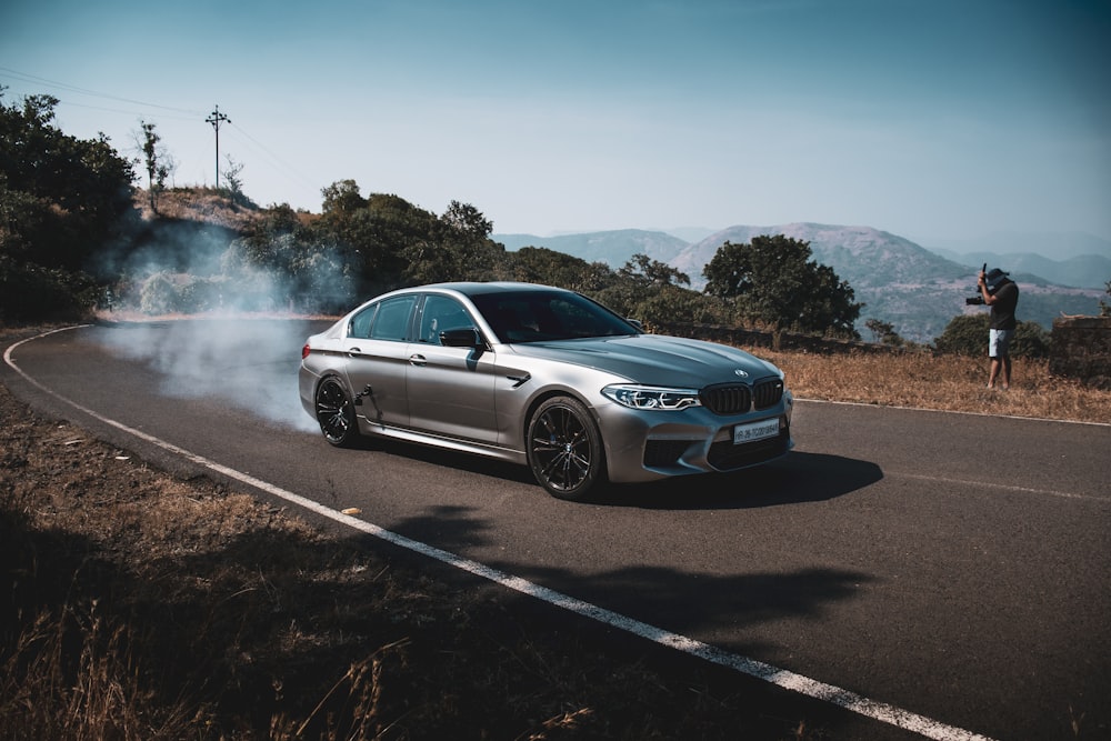 a silver car driving down a road with smoke coming out of it