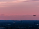A sunset silhouette of a small airplane soaring above rolling hills.