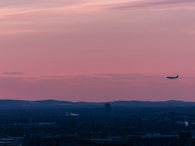 A sunset silhouette of a small airplane soaring above rolling hills.