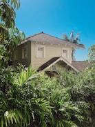 Front view of a two-story Bali-style house with lush tropical landscaping.