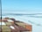 A view from a ship’s deck loaded with colorful shipping containers floating through icy waters. The horizon shows a vast expanse of frozen sea with patches of open water. The sky is clear with a light blue color.