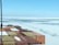 A view from a ship’s deck loaded with colorful shipping containers floating through icy waters. The horizon shows a vast expanse of frozen sea with patches of open water. The sky is clear with a light blue color.