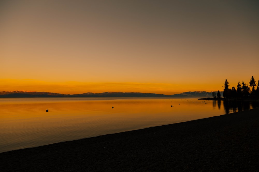 a sunset view of a lake with mountains in the distance