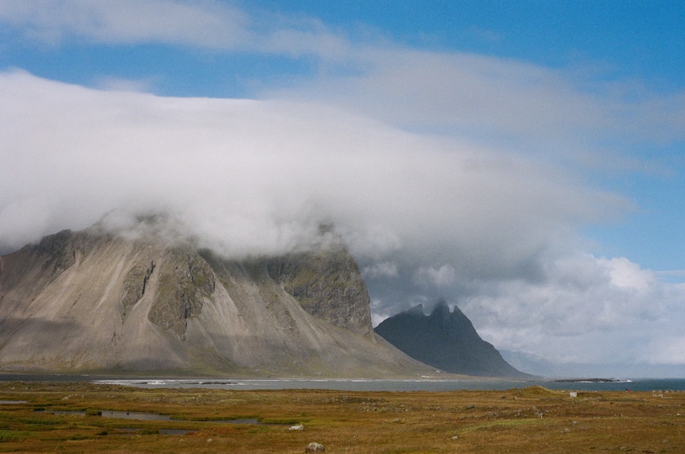 a mountain covered in clouds with a body of water in the foreground