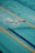 A swimmer is performing a butterfly stroke in an Olympic-sized swimming pool. The pool lanes are separated by floating lane markers, and the swimmer is wearing a white swim cap, goggles, and swimsuit. The water is a vibrant blue, with waves created by the swimming motion.