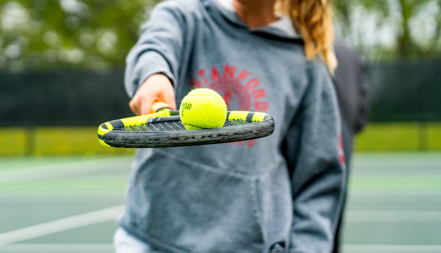 Raketinin üstünde top uzatan bir tenis öğretmeni