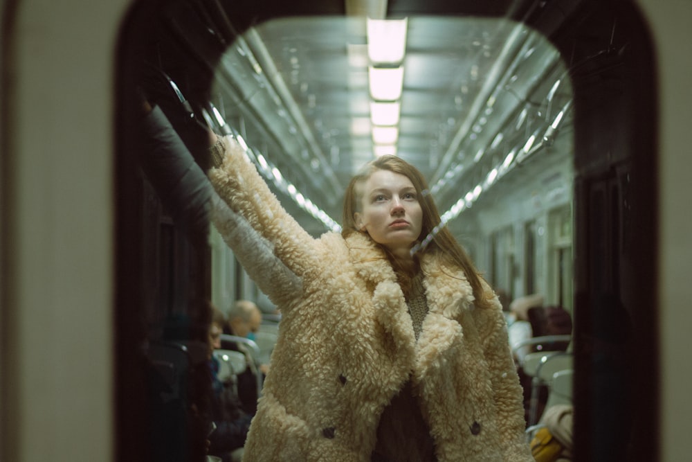a woman in a fuzzy coat is standing on a train
