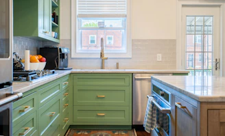 A sleek modular kitchen featuring dark green cabinetry with gold accents and a marble countertop.