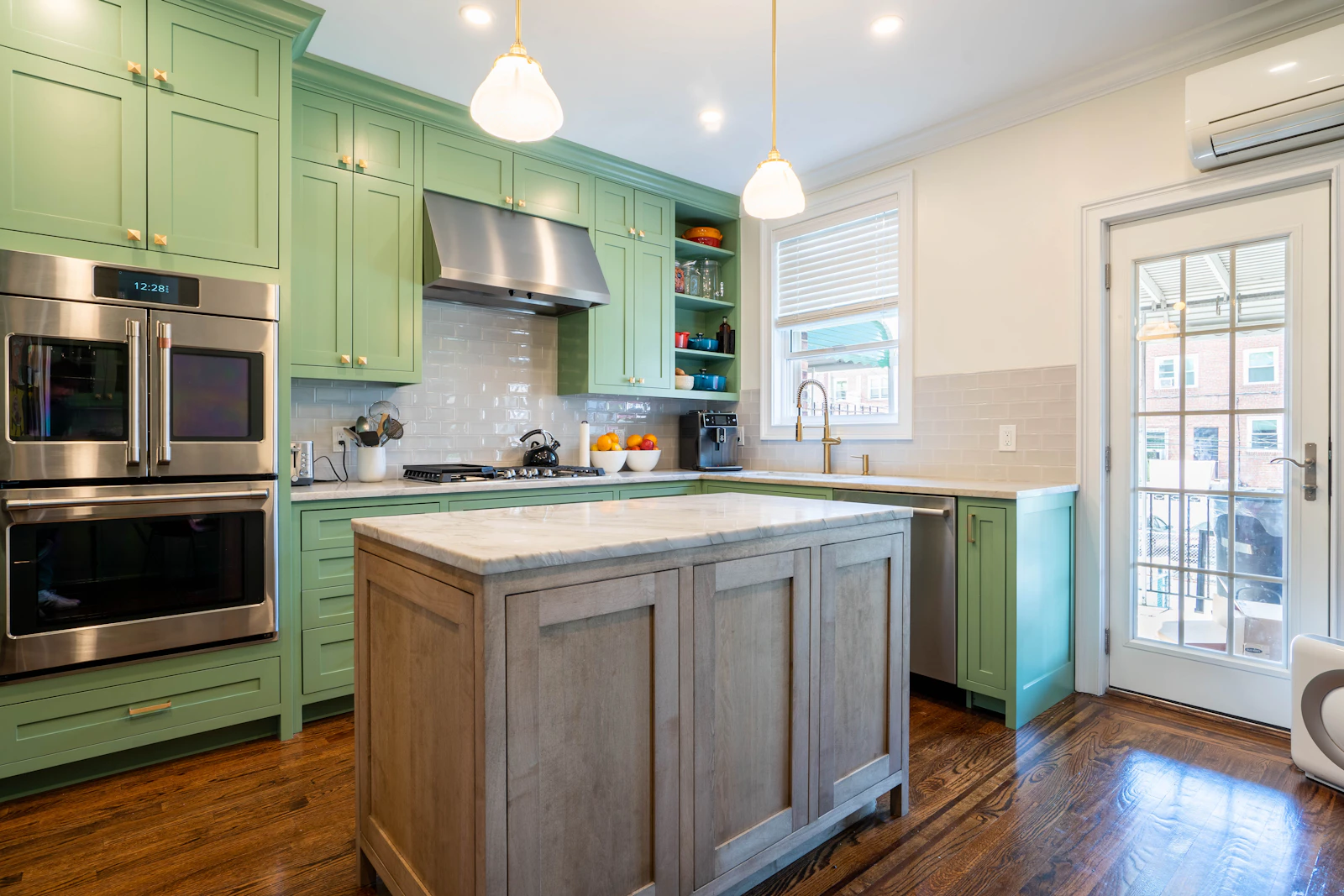 Sage-green shaker kitchen with brass faucet, schoolhouse pendants, and a stained wood island with marble top