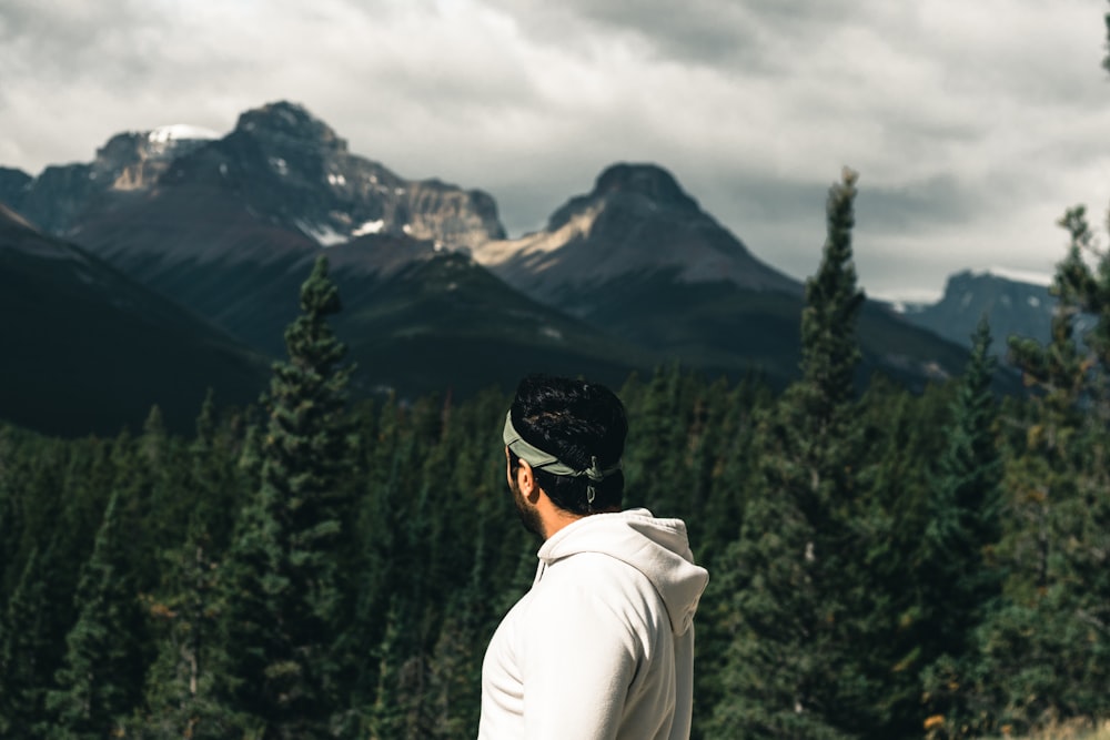 a man standing in front of a forest with mountains in the background