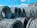 Large coils of steel cables are stacked together outdoors. The cables are neatly wound and secured with metal bands. Power lines and a clear blue sky with scattered clouds are visible in the background.